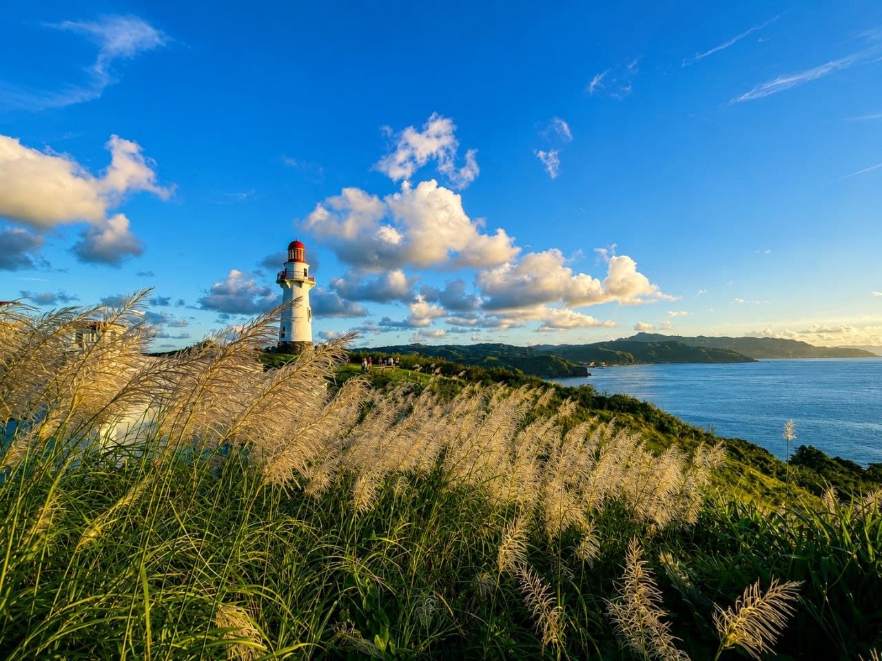 A lighthouse resting among green Batanes hills beside the ocean